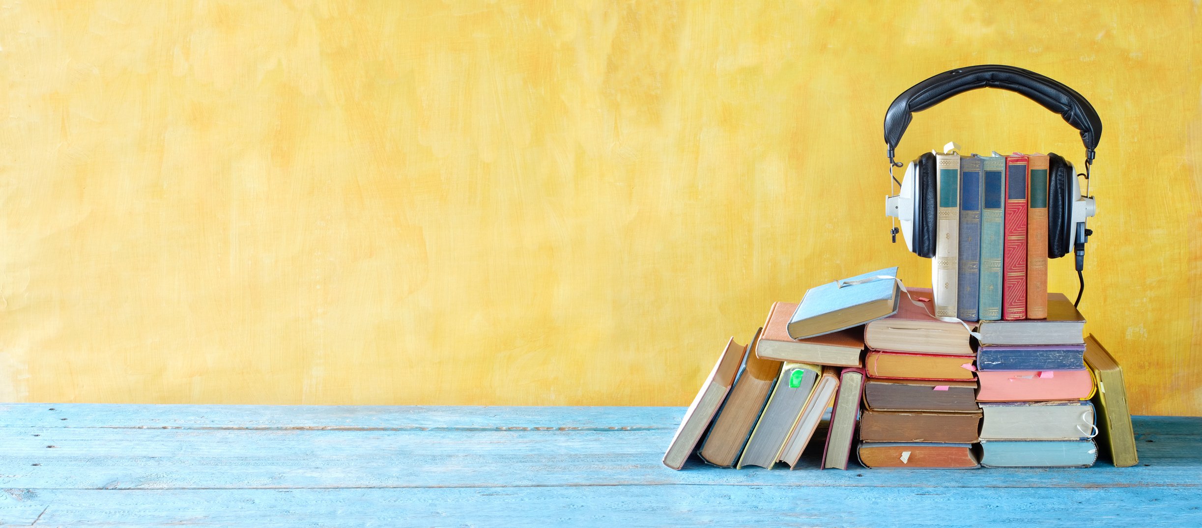 audio book concept with large heap of books and vintage headphones, panoramic, good copy space